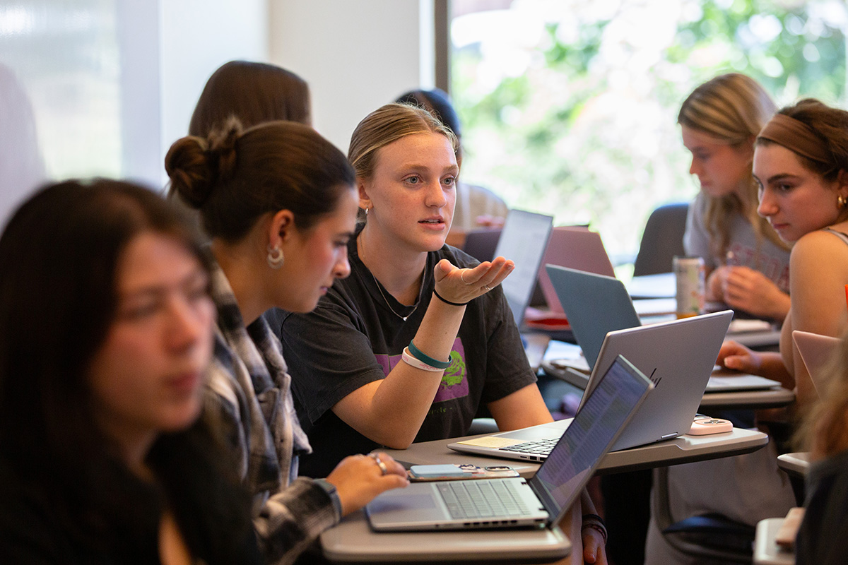 A student gestures and speaks while working on a group project in class. 